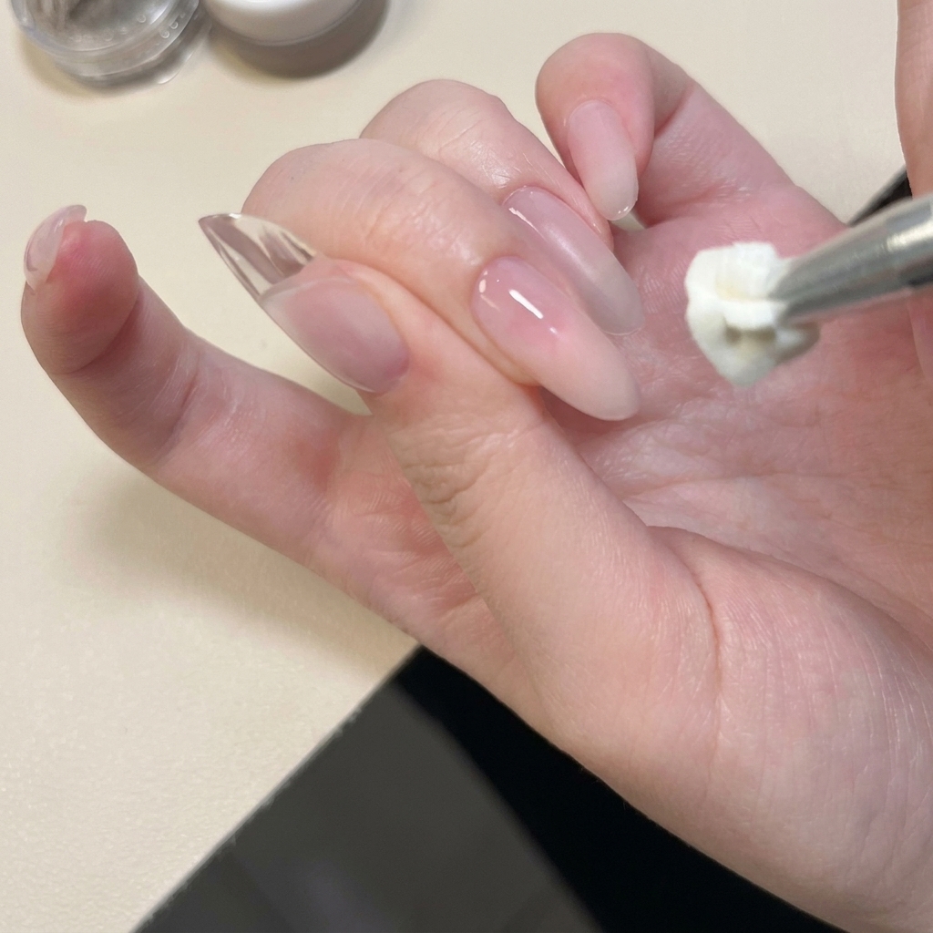 A close-up of a metal tool applying and patting white solid gel onto the tip of a natural nail.