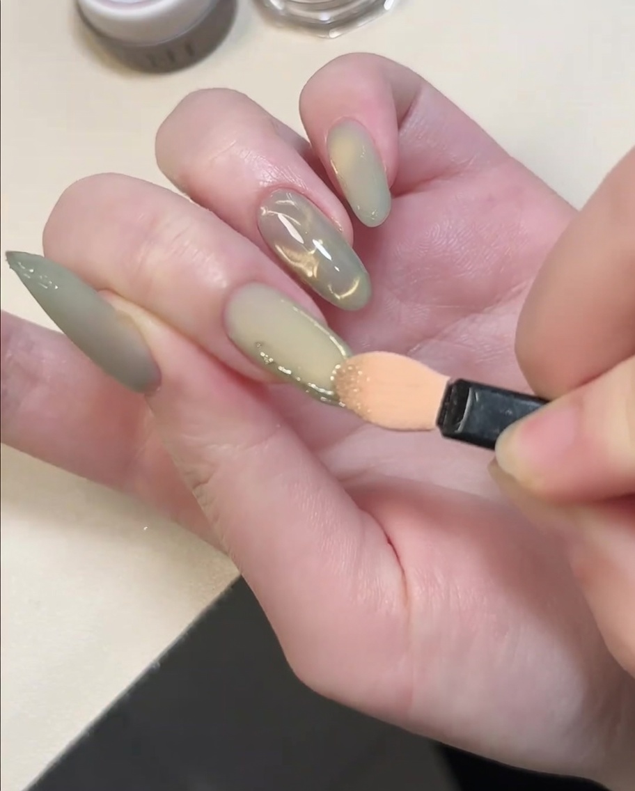 An eyeshadow applicator tip rubbing gold chrome powder onto raised 3D gel lines on a nail.