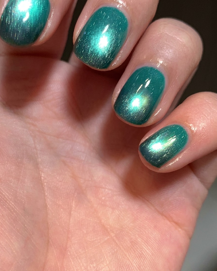 A brush applying a coat of bright lake-green cat-eye gel polish over a nail that has a black tip.