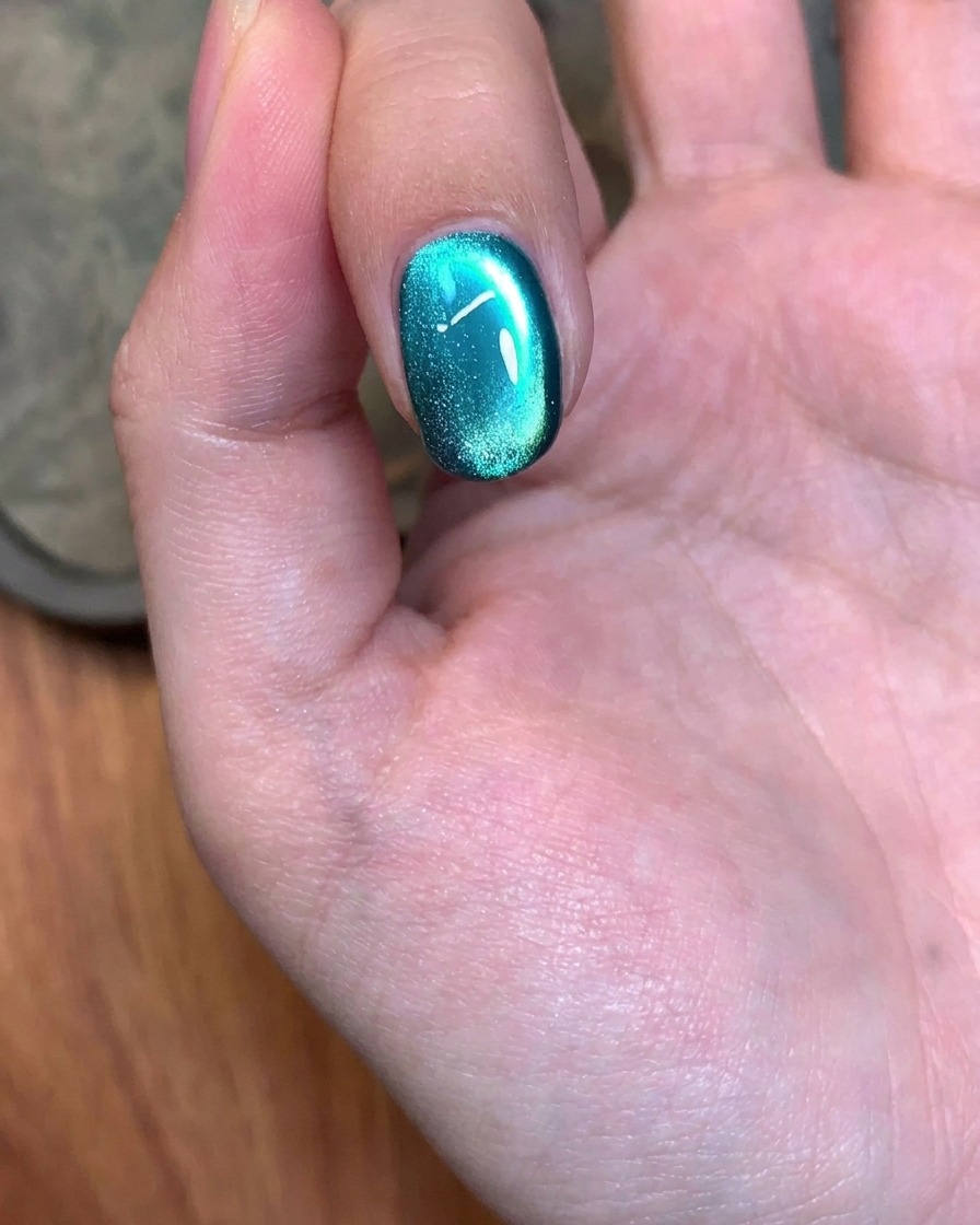 A magnetic tool being used in a circular motion over a green gel-painted nail to adjust the shimmer.