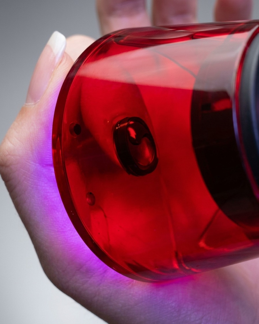 A close-up of a hand holding a red, compact UV/LED nail lamp directly over a finger to cure the applied gel polish.