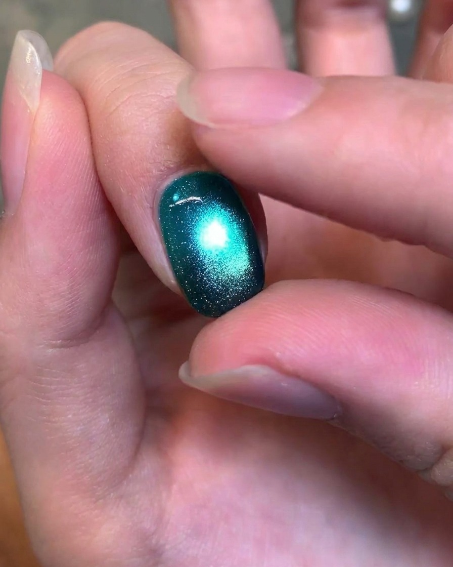 A close-up view of a finger gently testing the texture of a finished, glossy deep green cat-eye gel nail.