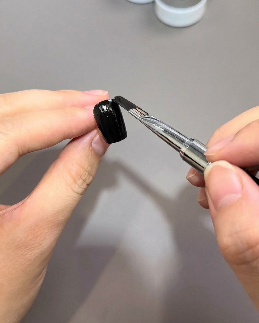 A nail brush applying a smooth coat of black gel polish onto a prepped nail surface.