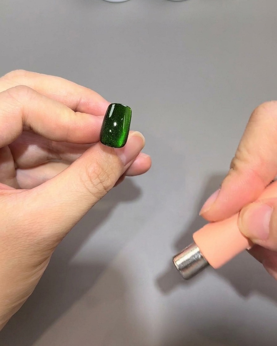 A cylindrical magnet held parallel to the right edge of a fingernail to continue shaping the magnetic glow.
