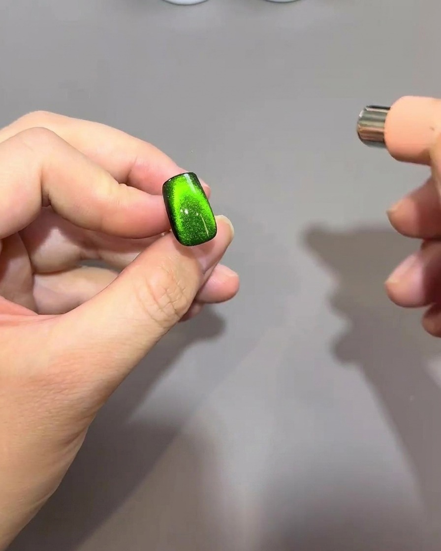 A magnet performing a C-curve motion at the nail tip to concentrate magnetic particles into a rounded, bead-like shape.