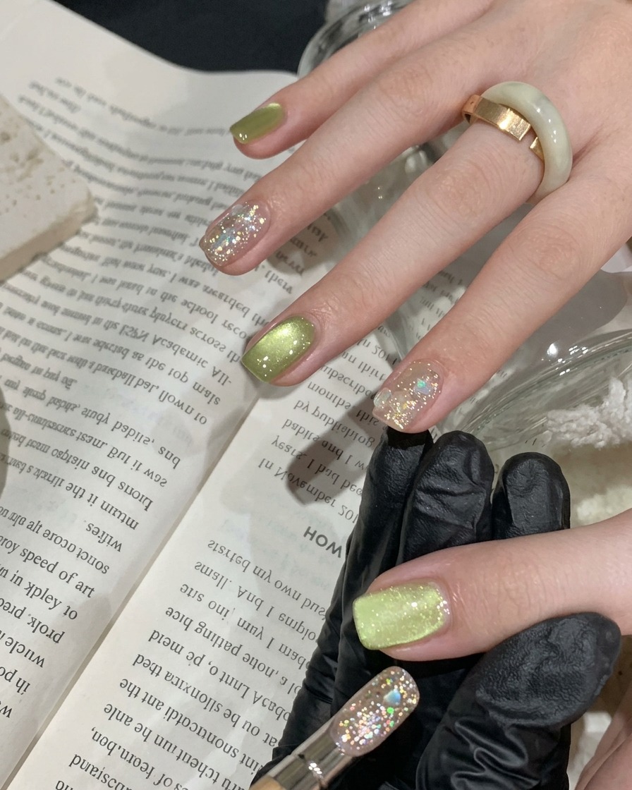 A brush applying a thin layer of vibrant green cat-eye gel polish onto a natural nail.