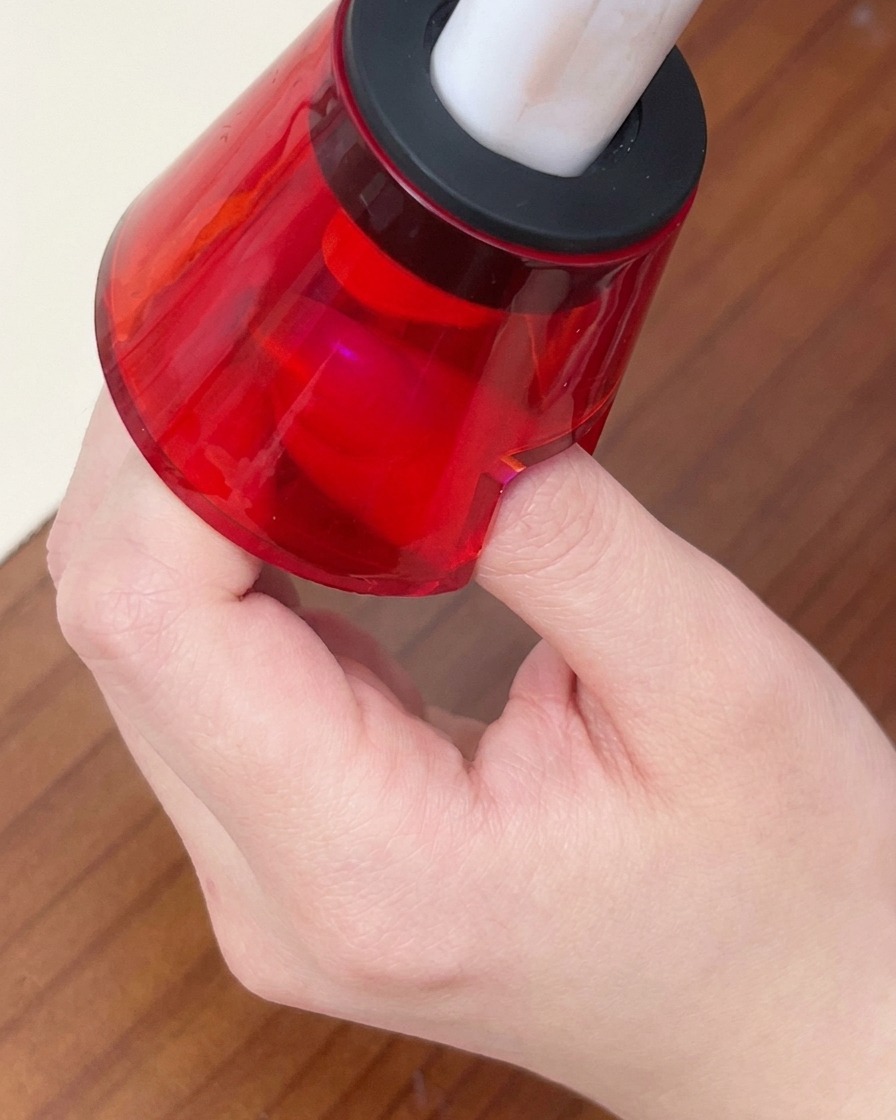 A finger placed under a small red handheld LED lamp to cure the gel polish.