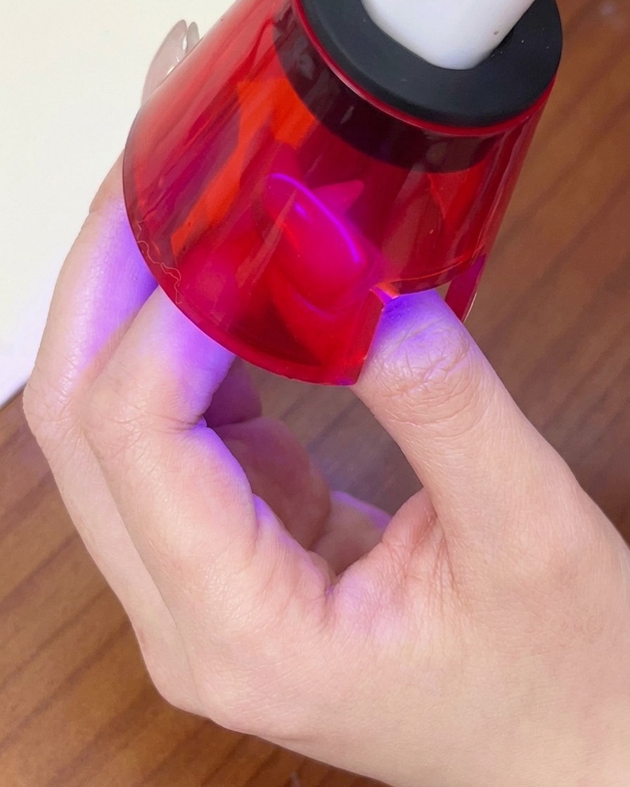 A finger curing under a red handheld LED lamp to set the magnetic gel design.