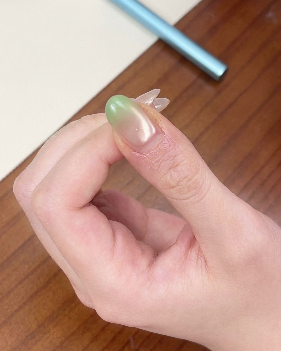 A fingernail with a green gradient tip positioned under a portable red mini UV lamp.