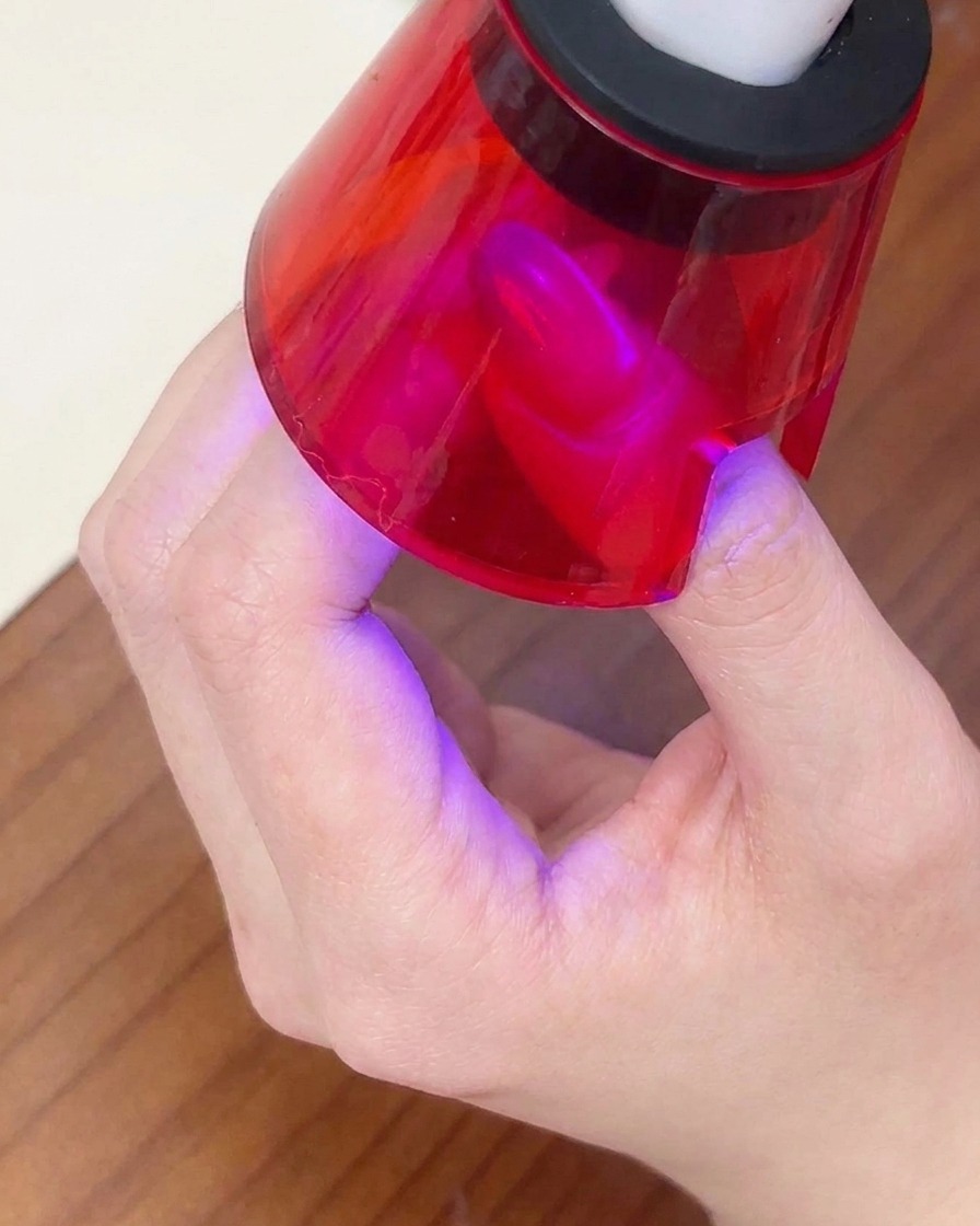 A finished nail being cured under a small red portable UV lamp.