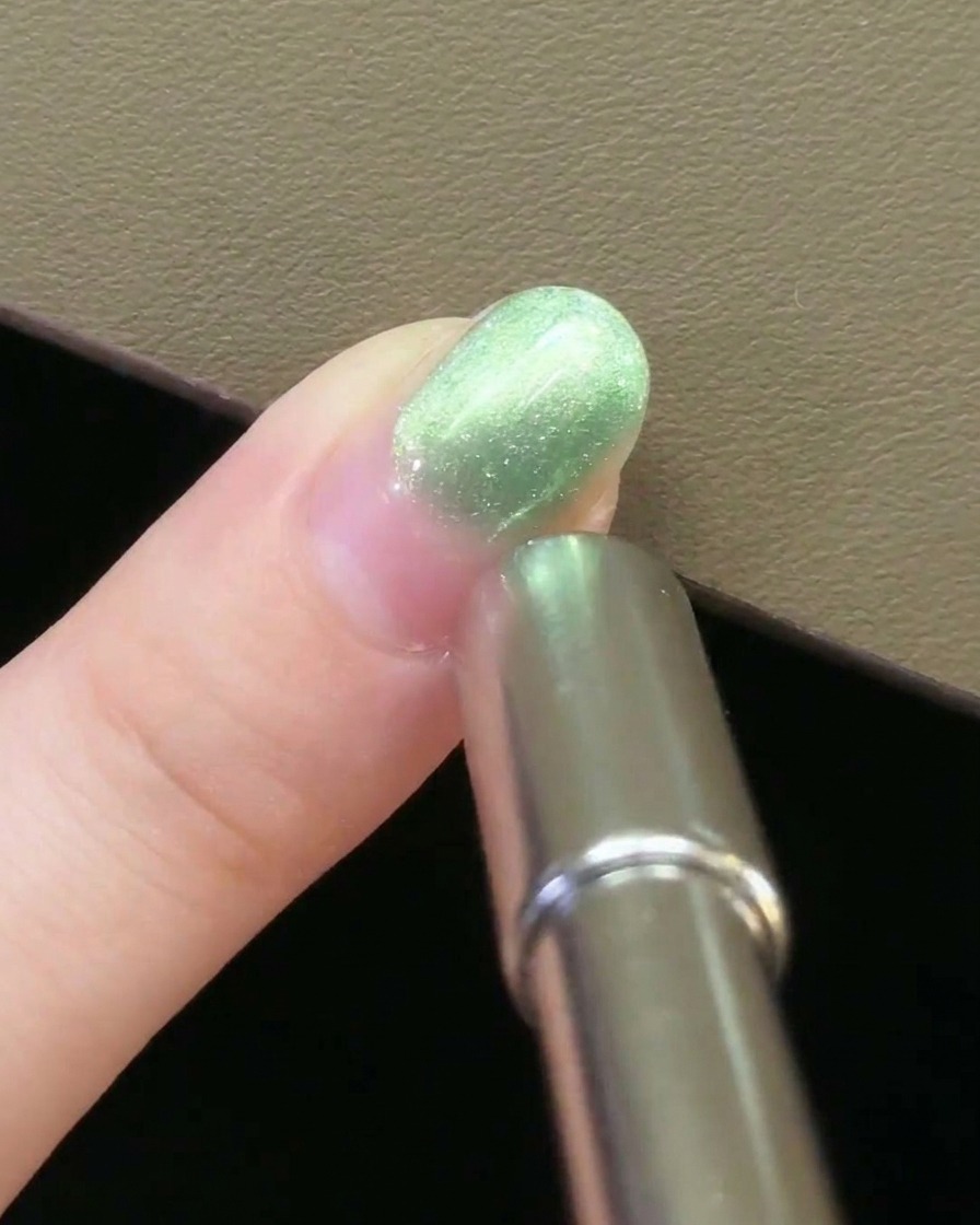 A metal nail magnet held parallel to the side of a fingernail coated in green magnetic gel.