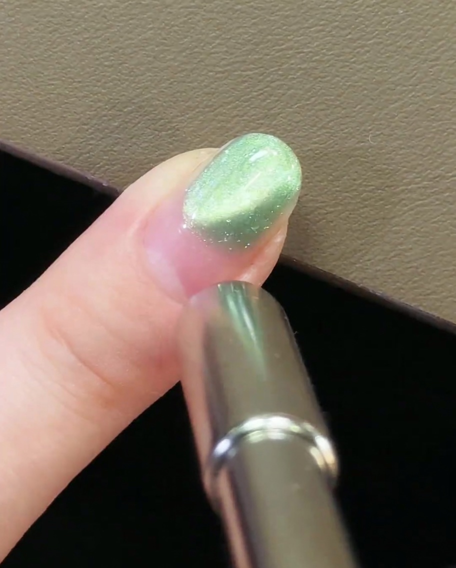 A metal nail magnet positioned at the cuticle area of a nail with green magnetic cat-eye gel.