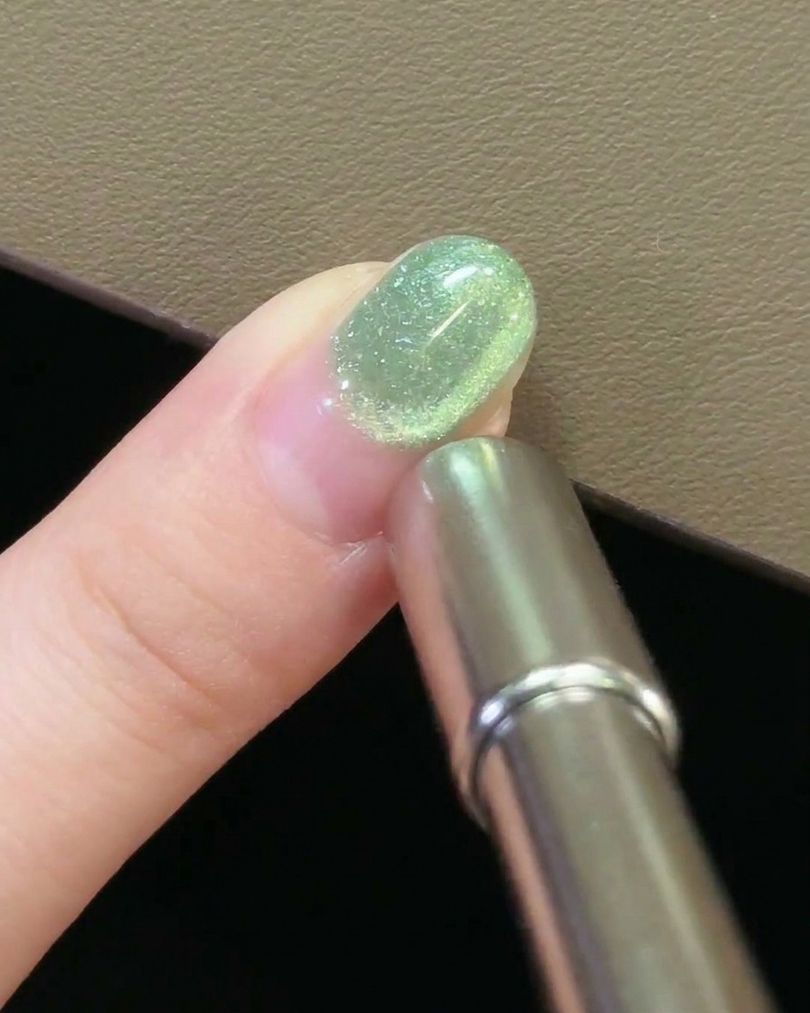 A close-up view of a magnet hovering over a nail, creating a circular movement in the cat-eye gel.