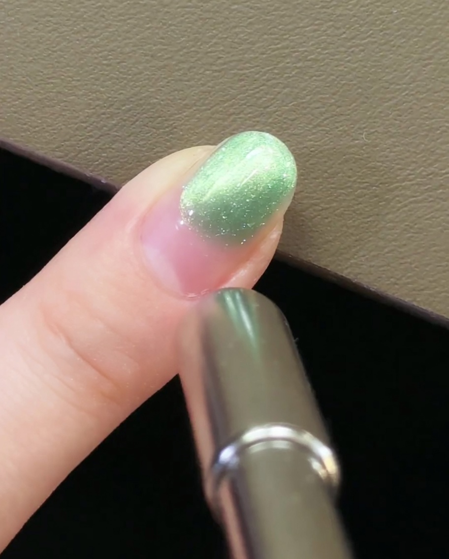 A hand pulling a magnetic tool away from the fingernail to lock in the cat-eye pattern.
