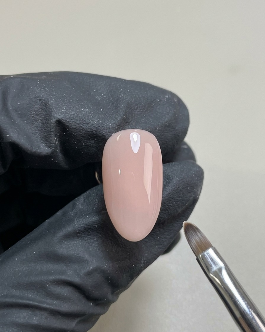 A single nail with a smooth, translucent nude gel base coat, cured and ready for nail art.