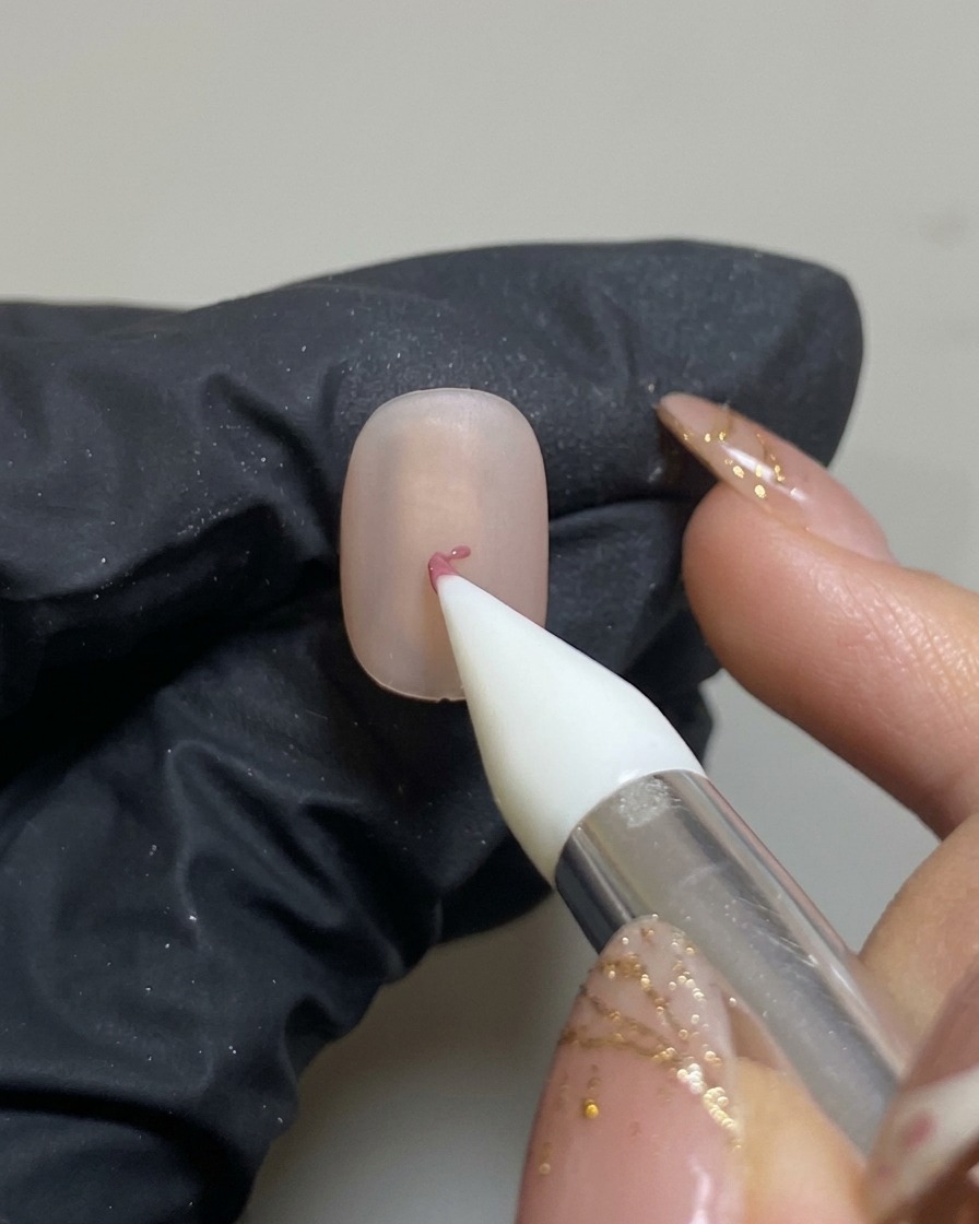 A silicone nail tool placing a small dot of pink gel in the center of a matte-finished nude nail.