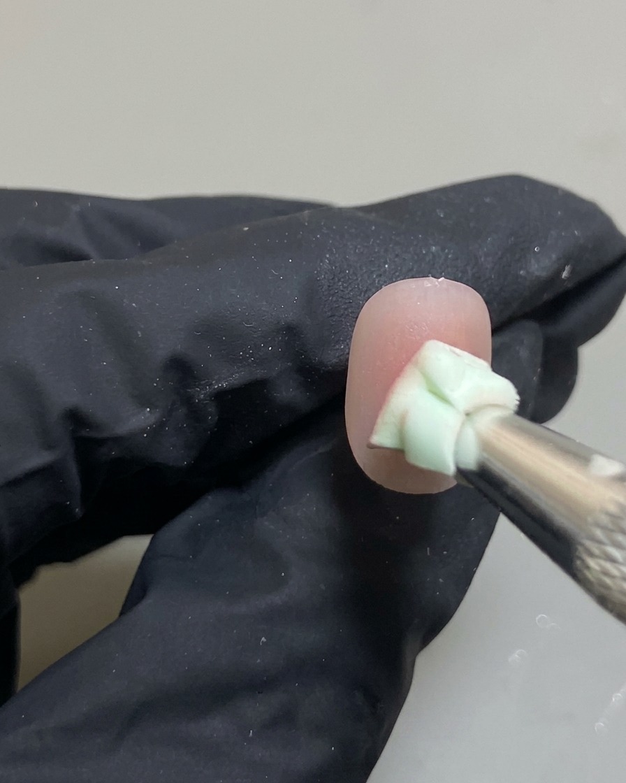 A close-up of a nail with a sponge tool blending a pink gel dot into an ombre blush effect.