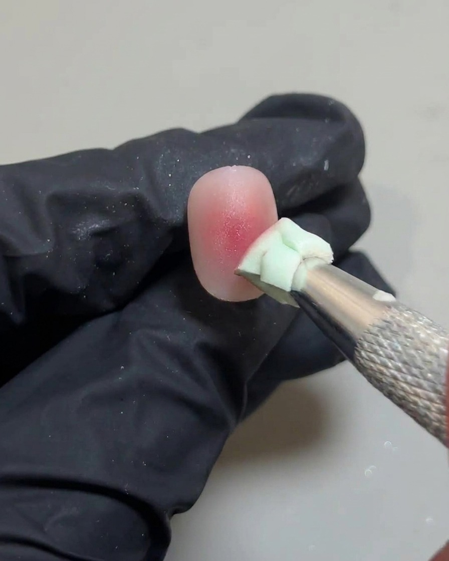 A sponge tool lightly tapping the center of the nail to blend the final pink gel dot.