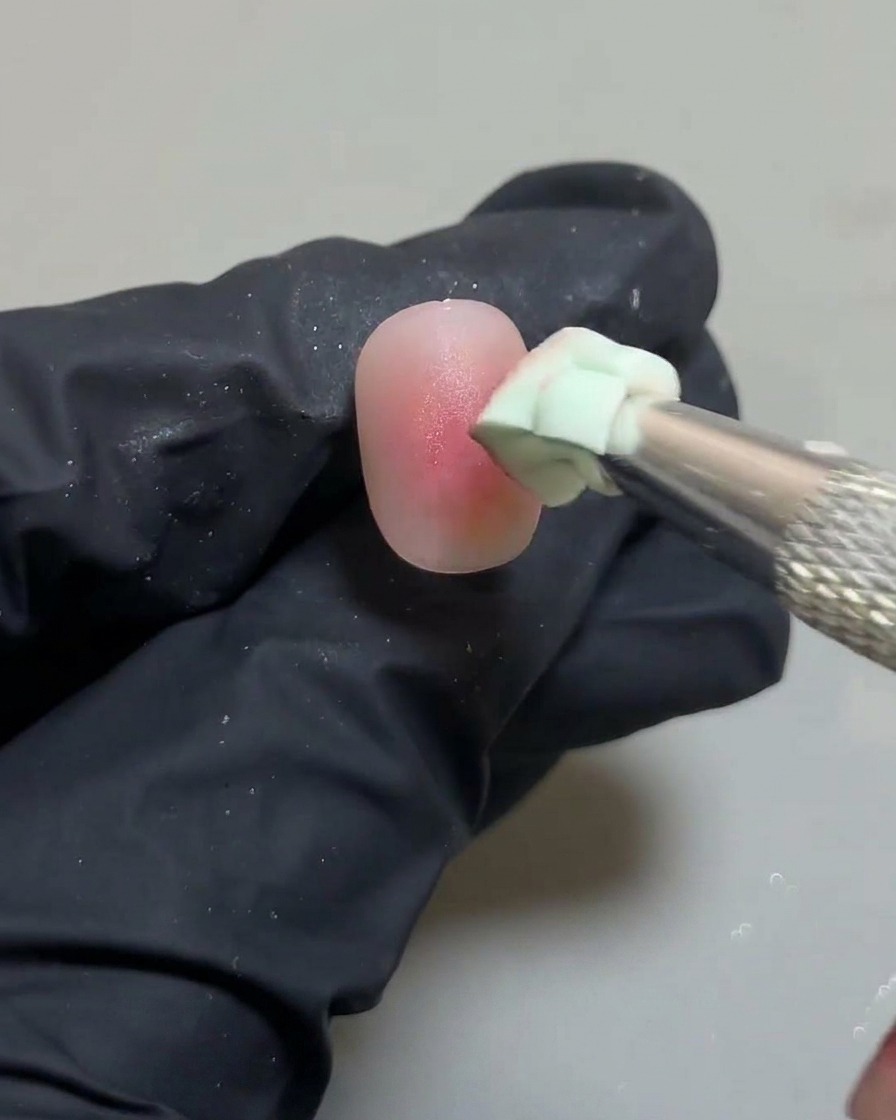 A close-up of the sponge tool perfecting the edges of the ombre blush nail design.