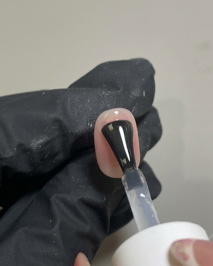 A brush applying a clear, glossy top coat over the finished blush nail art.