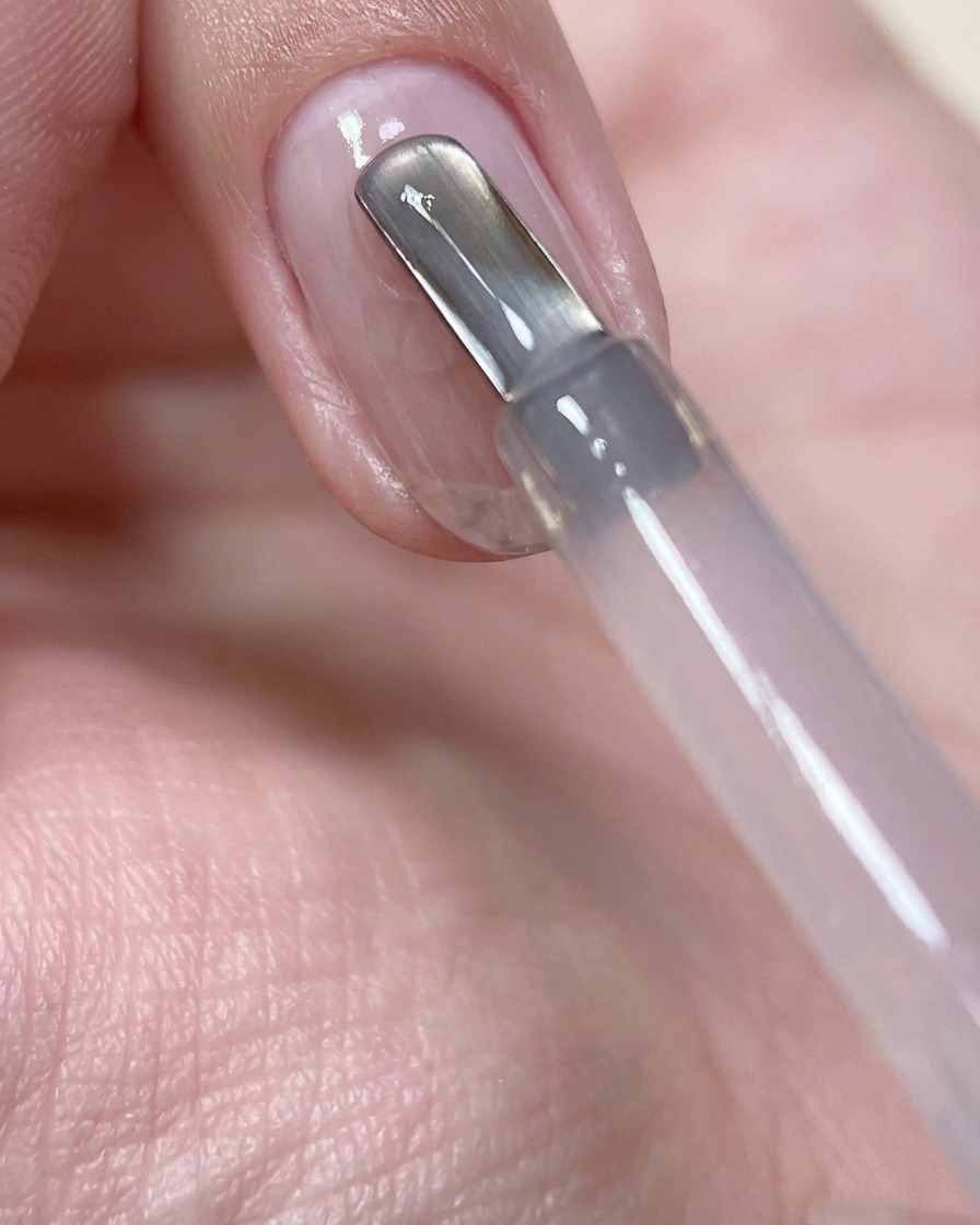 A close-up of a nail brush applying a bead of sheer pink builder gel to the center of a prepped natural nail.