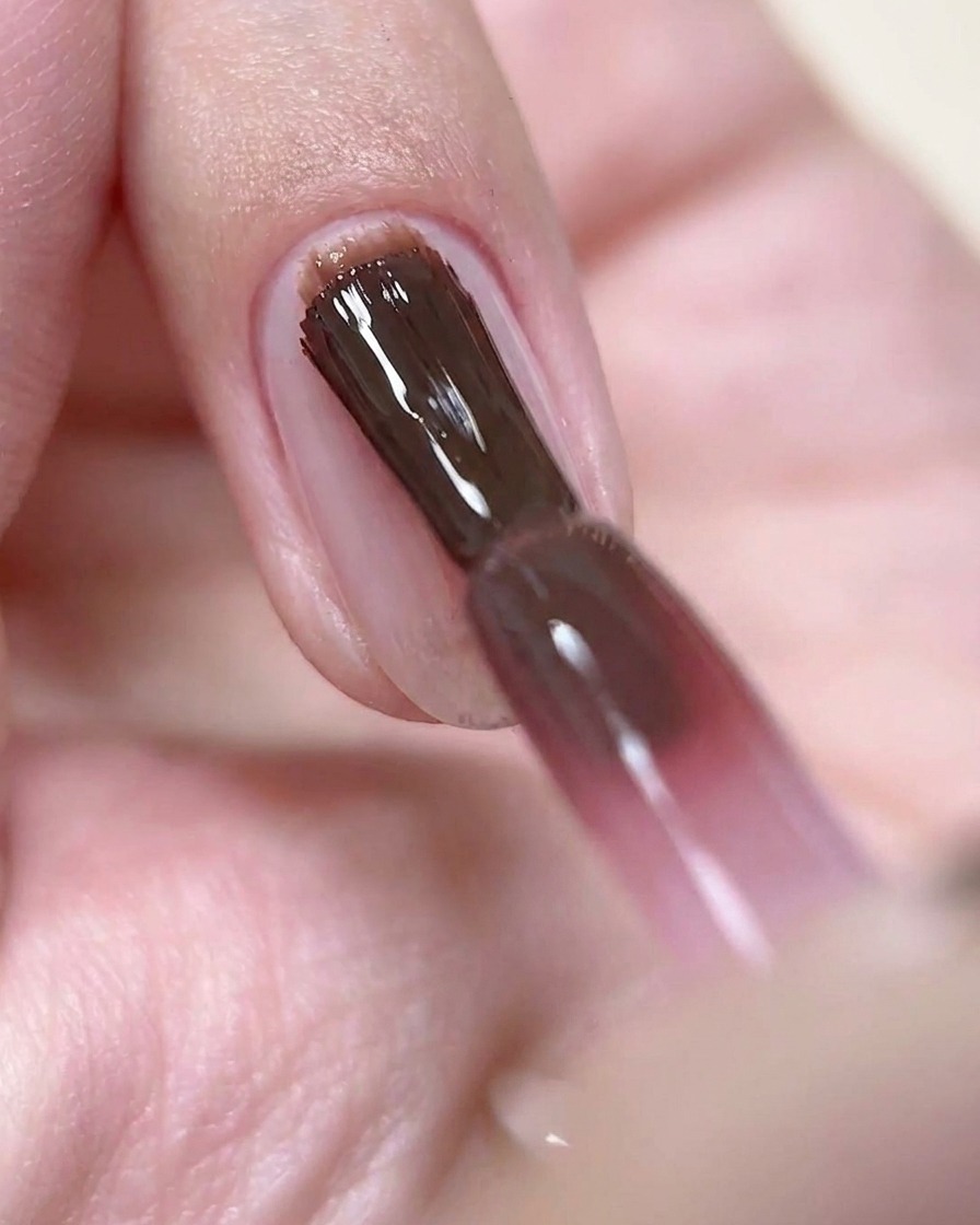 A nail brush applying a thin layer of deep rose-wine colored gel polish onto a prepped nail.