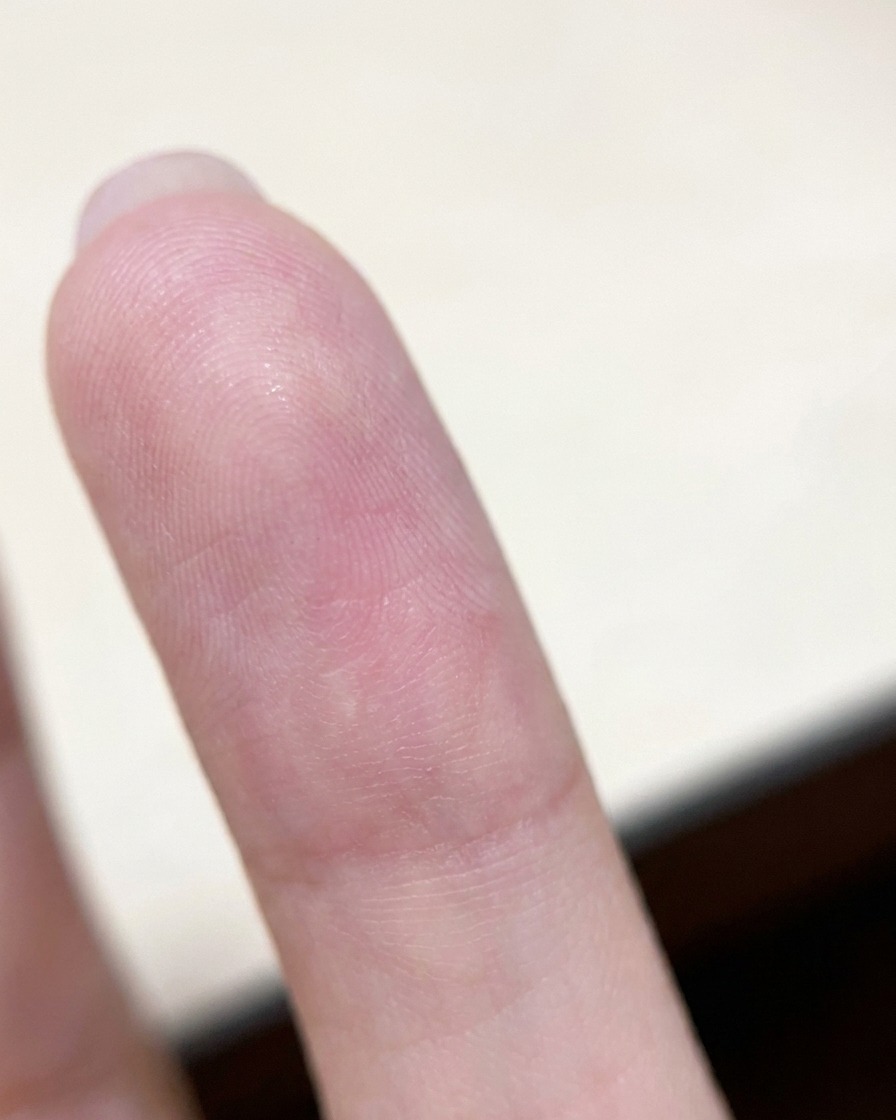 A finger turned upside down showing the fingerprint pad, held still to allow gravity to pull the wet nail gel towards the center of the nail.
