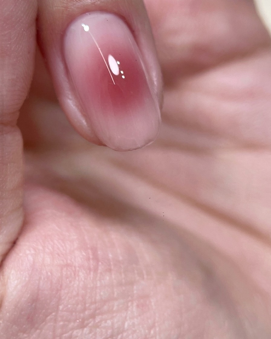 A close-up of a finger with a blushing rose-wine gel center placed inside a UV nail lamp for curing.