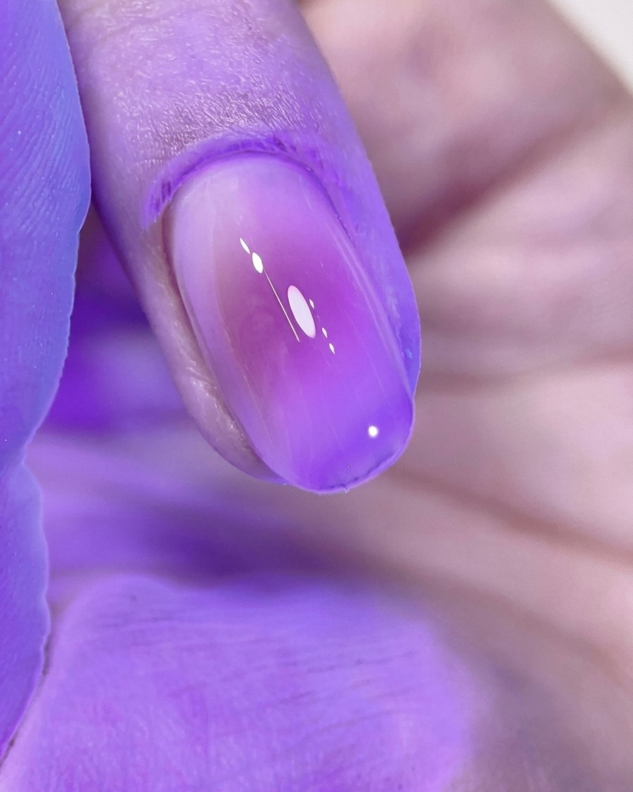 A beautifully manicured pink blush nail curing under the bright purple light of a UV/LED nail lamp.
