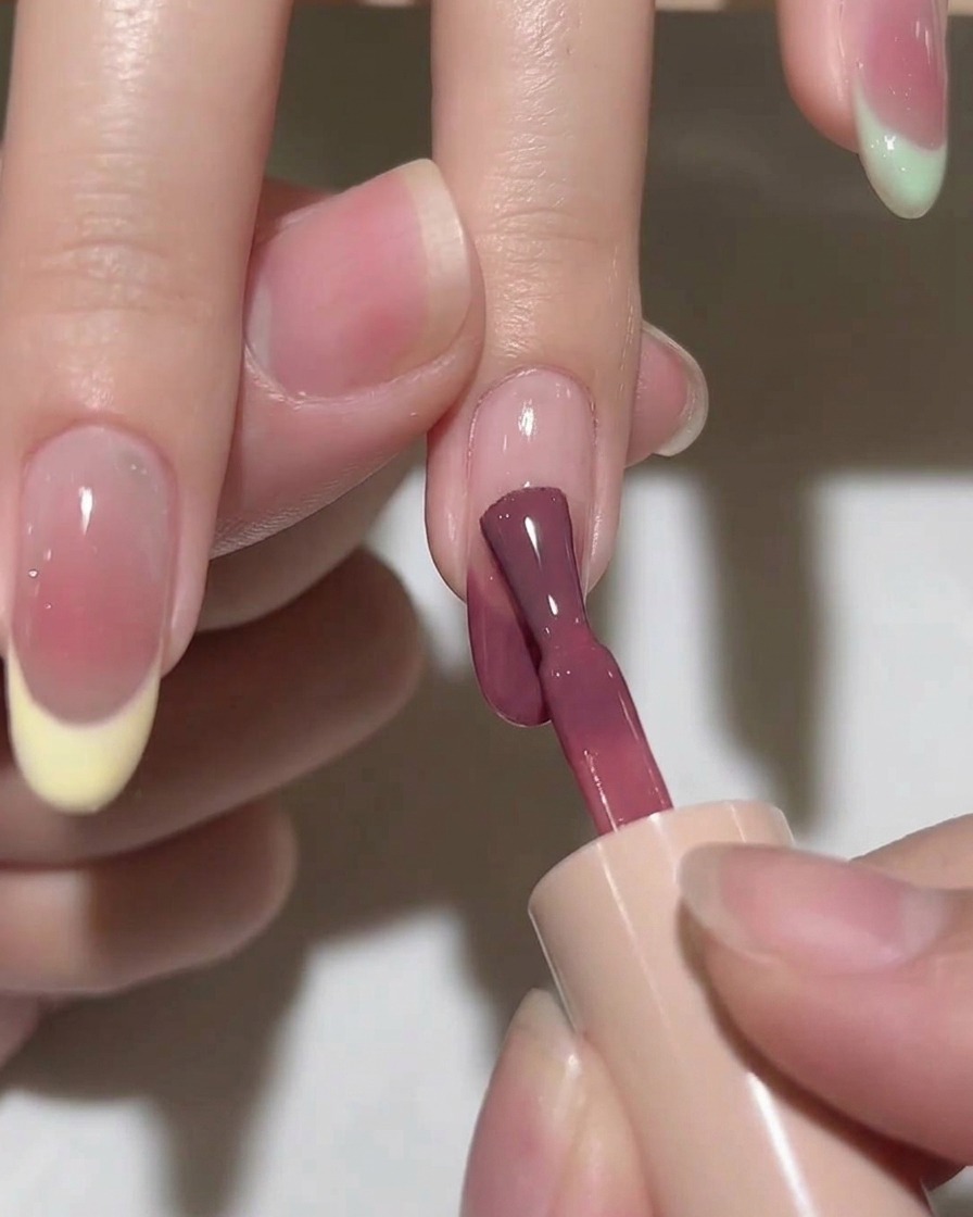 A brush blending a drop of pink gel on a nail, creating a soft, diffused circular color effect.