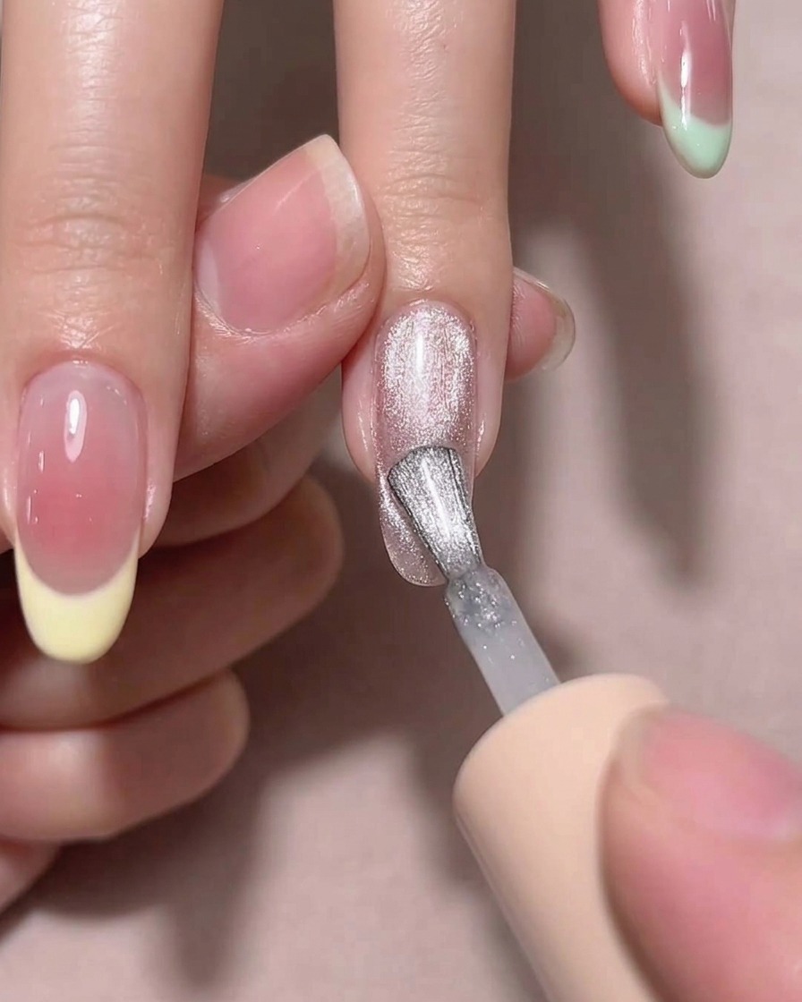 A magnetic tool held near a wet polish-coated nail to create a diagonal shimmer effect.