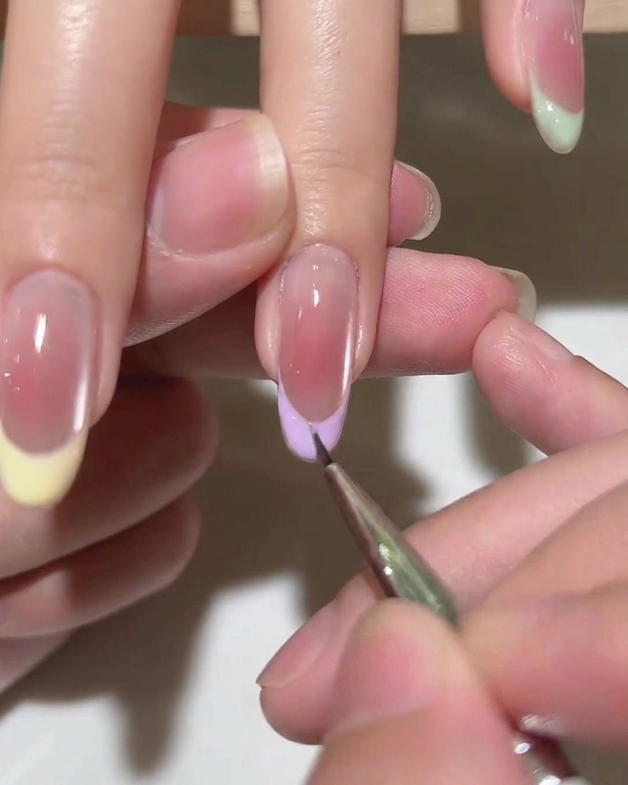 A brush applying a layer of clear top coat over a finished French tip manicure.