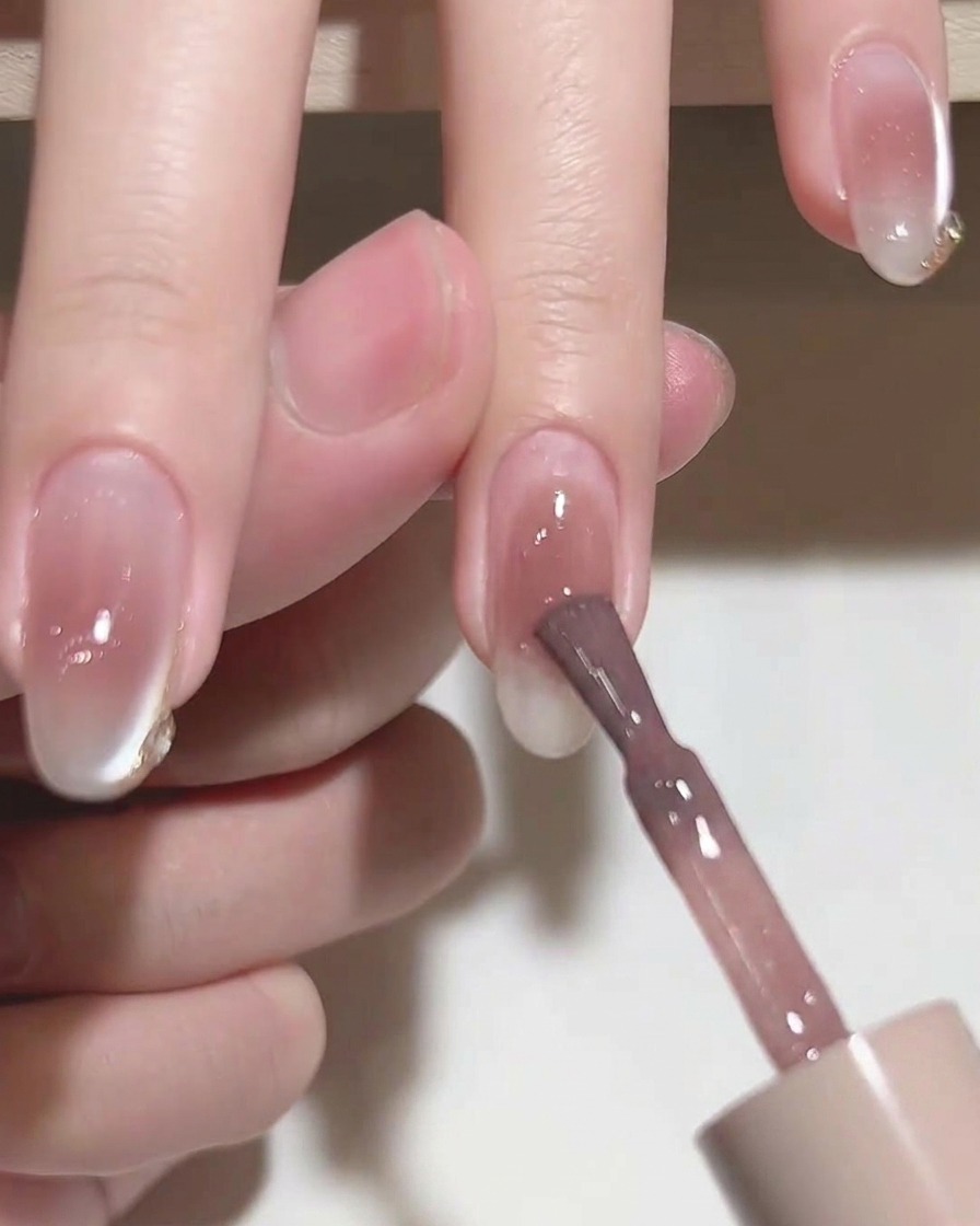 A flat brush smoothing out pink gel polish on a nail.