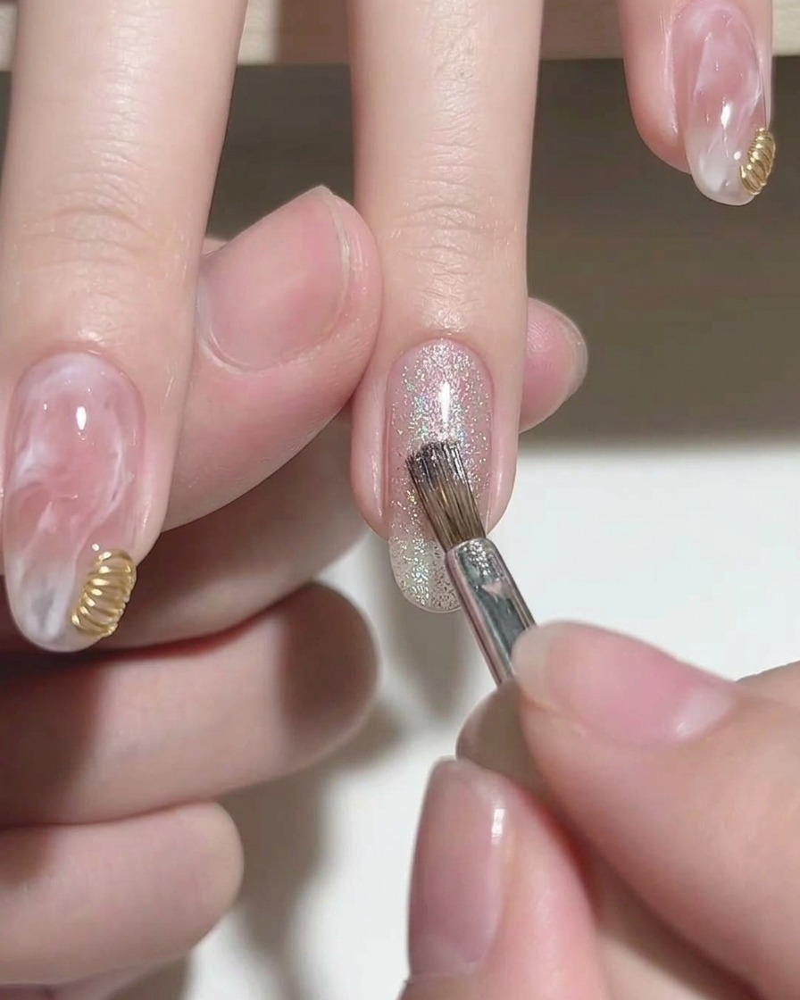 A brush applying silver sparkly cat-eye gel polish to the tip of a pink gel nail.