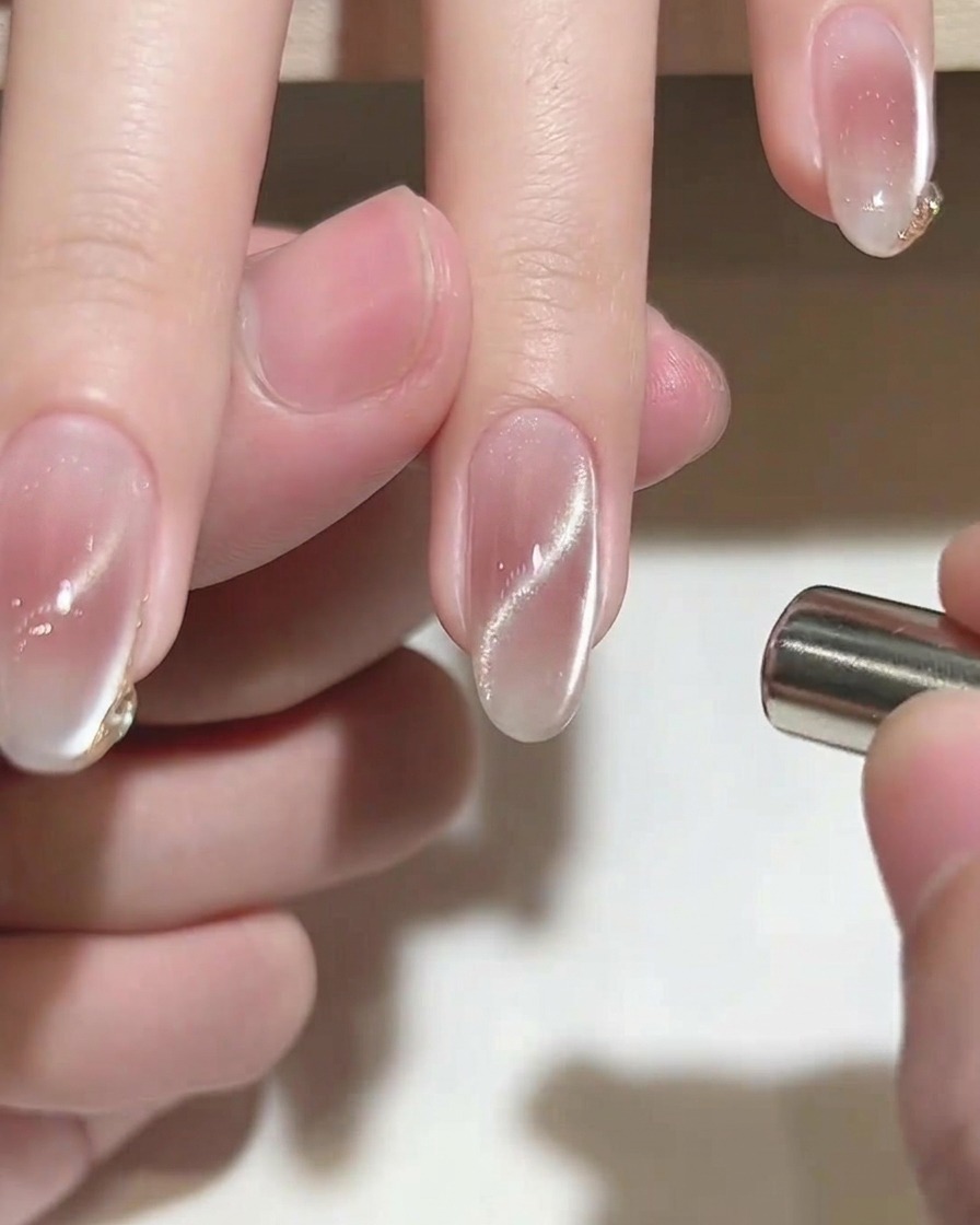 A fine liner brush adding a delicate gold accent to the tip of a pink nail.