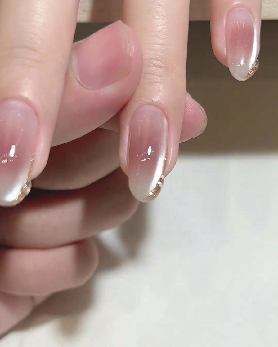 A brush applying a clear, glossy top coat over a nail featuring delicate gold tip details.