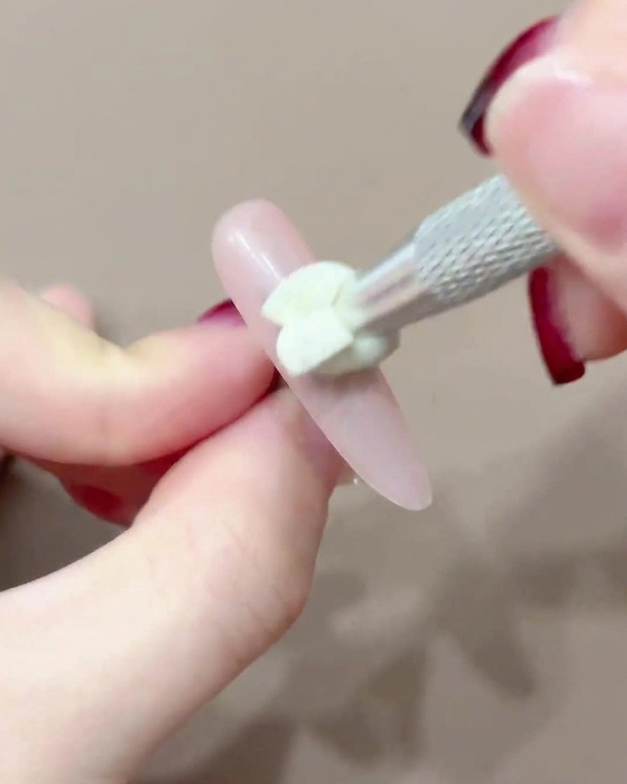 A silicone-tipped tool dabbing pink pigment onto the center of a nail.