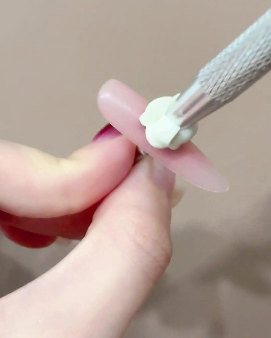 A brush applying a small, precise dot of pink blush gel to the center of a nail.