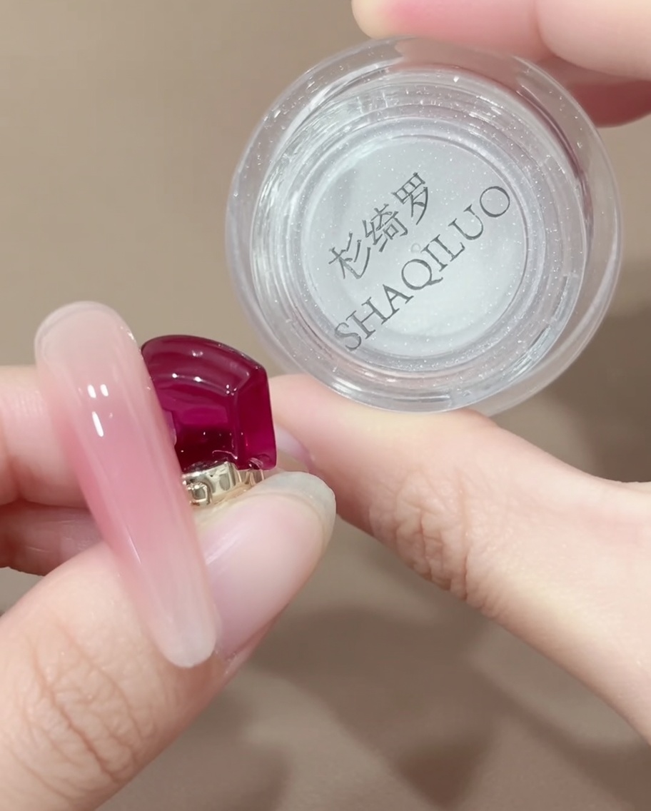 A silicone-tipped applicator tool picking up a small amount of iridescent chrome powder from a jar.