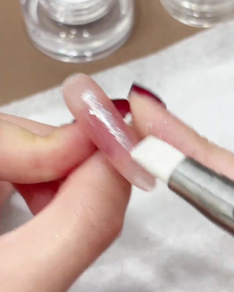 A silicone pen buffing iridescent chrome powder into the surface of a manicured nail.