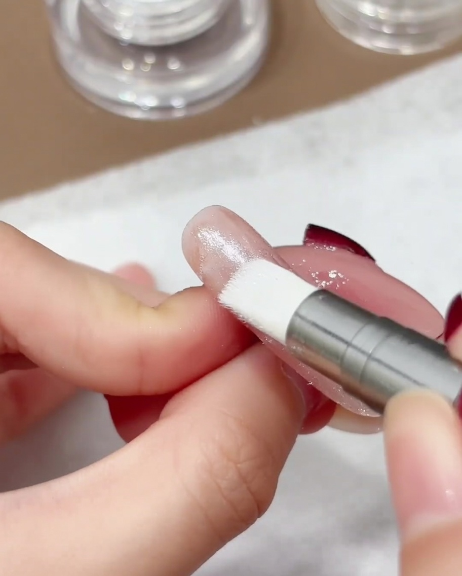 A close-up shot of a silicone-tipped applicator pen buffing iridescent aurora chrome powder onto a nail surface.