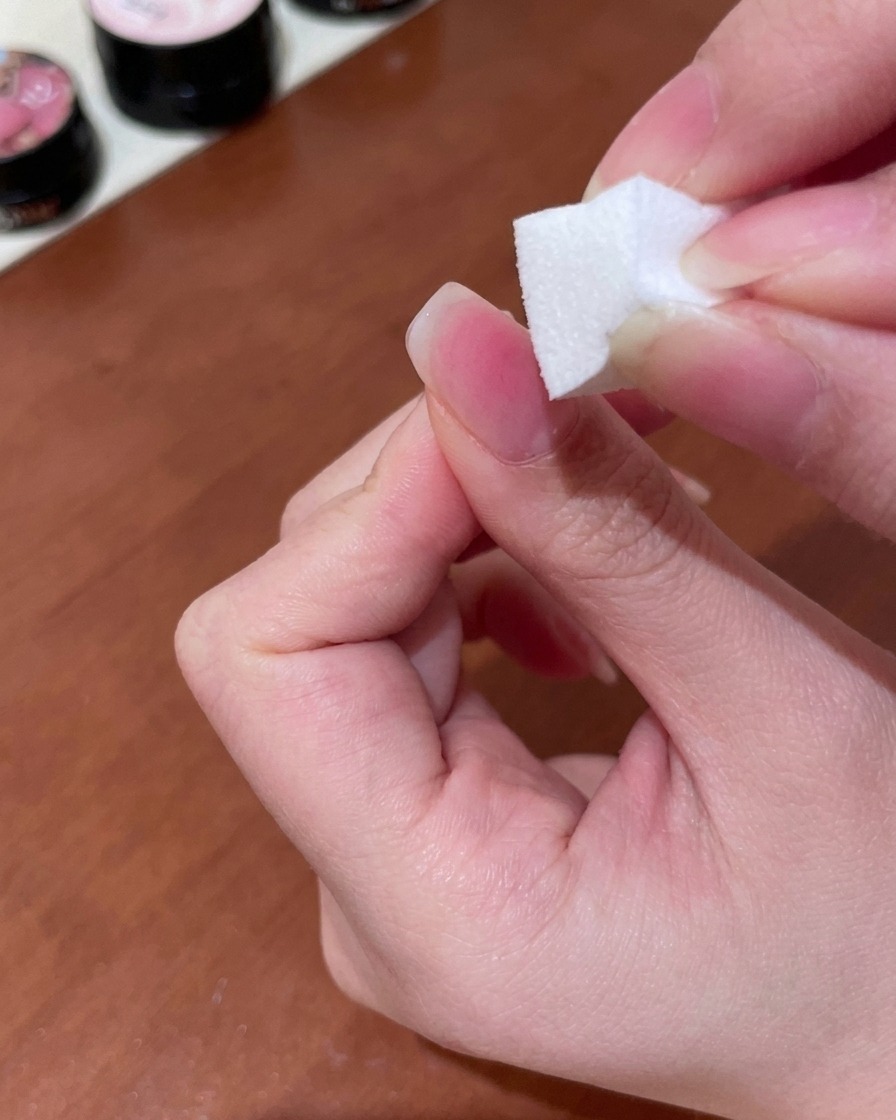 A makeup sponge being used to pat and blend peach gel into a soft gradient on the nail surface.
