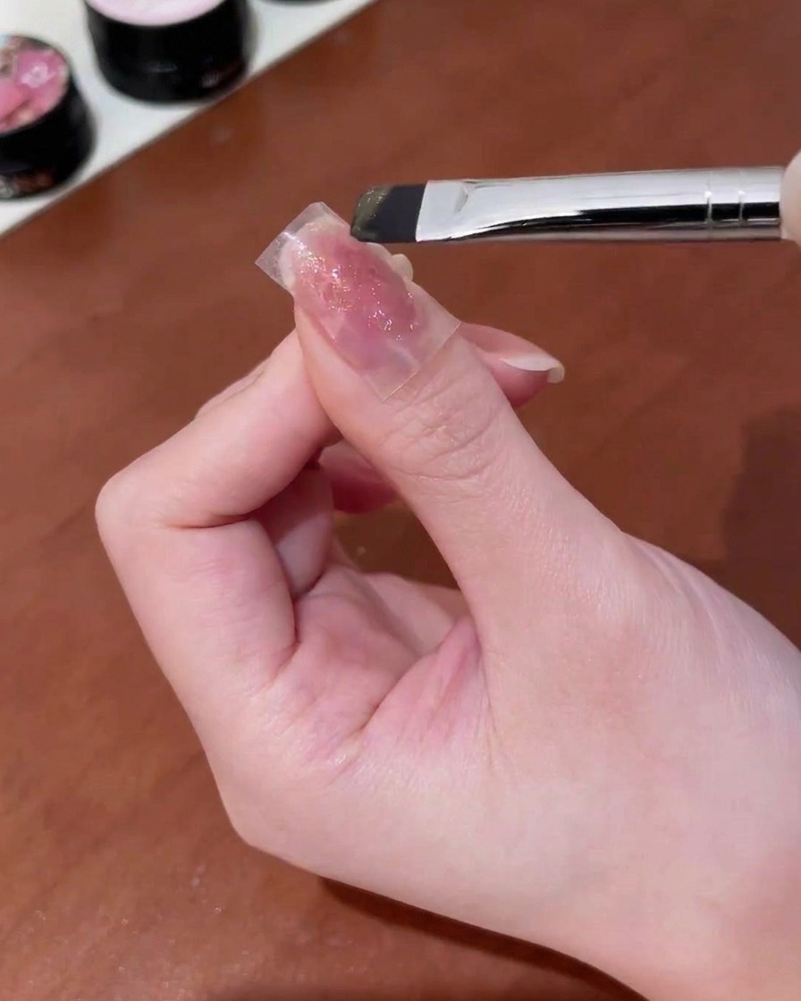 A brush applying gold cat-eye gel over a butterfly sticker on a nail.
