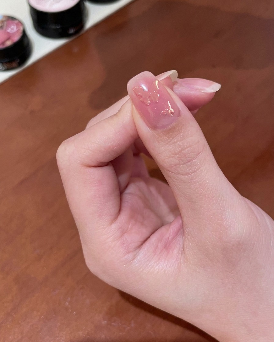 A close-up view of a hand holding a small cylindrical magnet over a fingernail coated in wet gold magnetic gel, revealing a shifting shimmer.