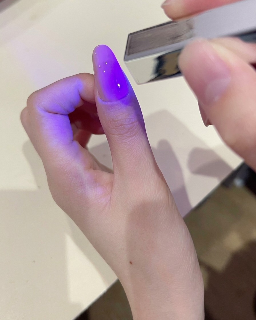 A hand using a lint-free wipe to clean the surface of a cured gel nail.
