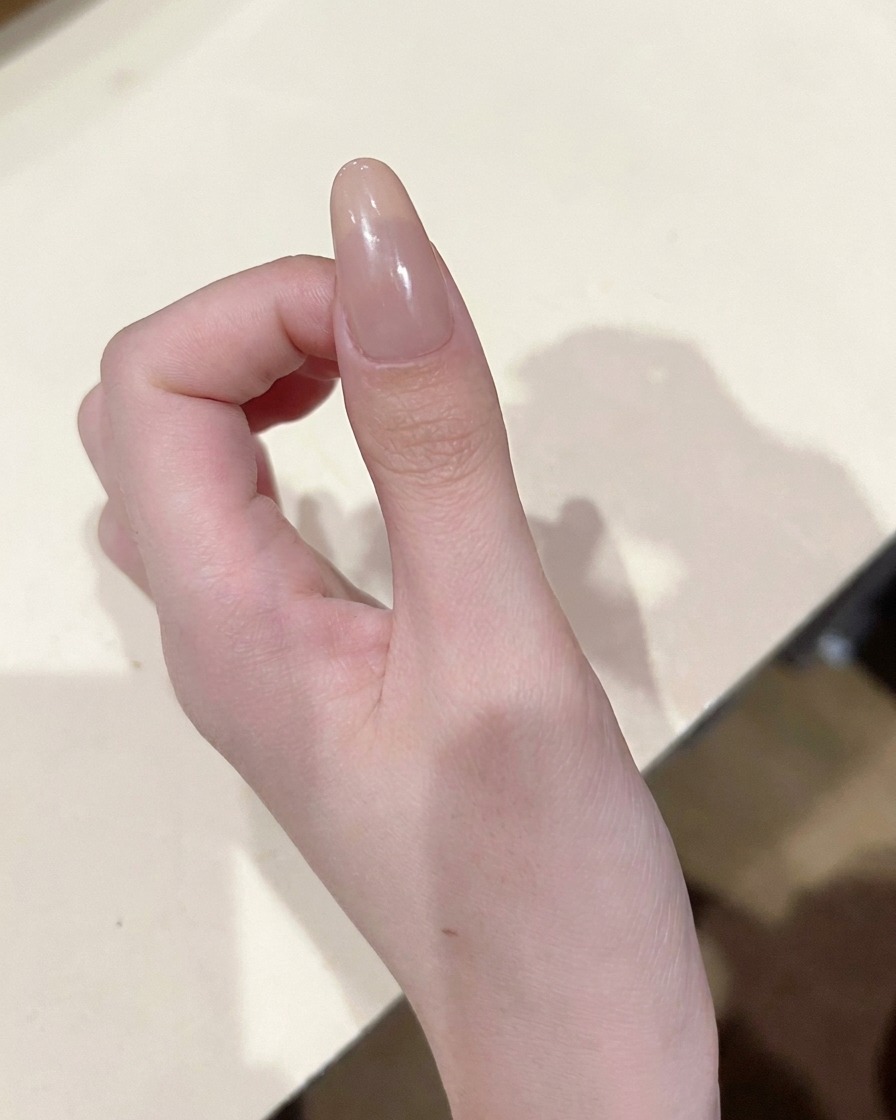 A close-up view of a detail brush placing a small, precise dot of pink-toned color gel in the center of a nude nail.