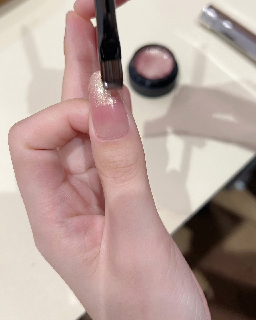 A small nail brush applying cat eye gel to the tip of a nail, blending it slightly downward.