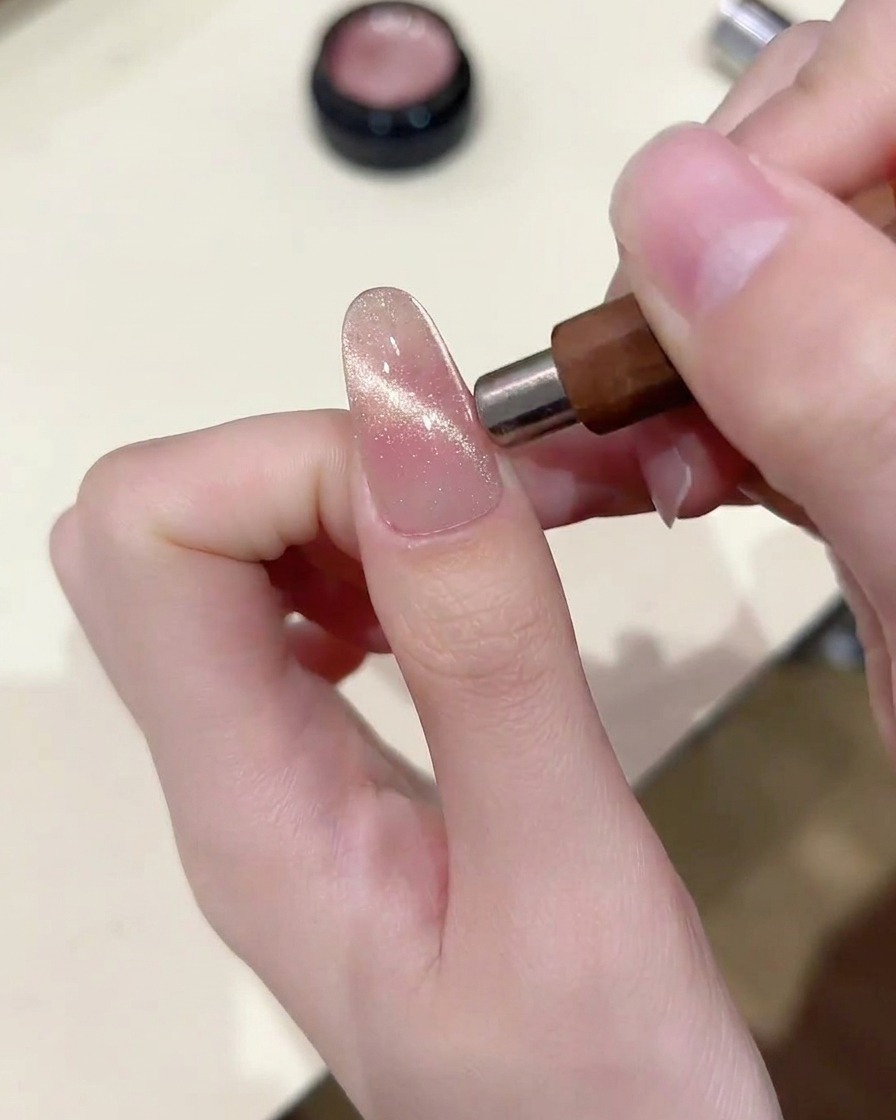 A magnetic tool held parallel to the nail, concentrating the cat eye particles into a horizontal band.