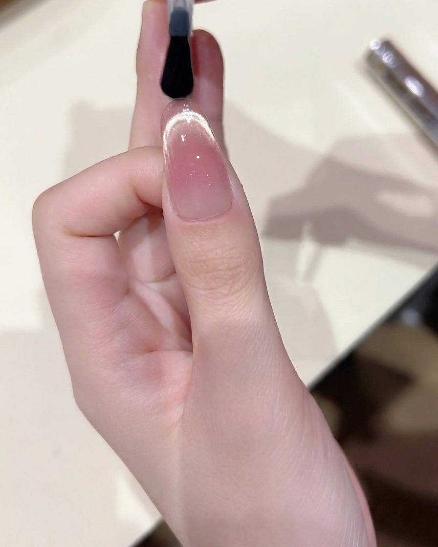 A brush applying a final, high-gloss top coat over the finished cat eye nail design.