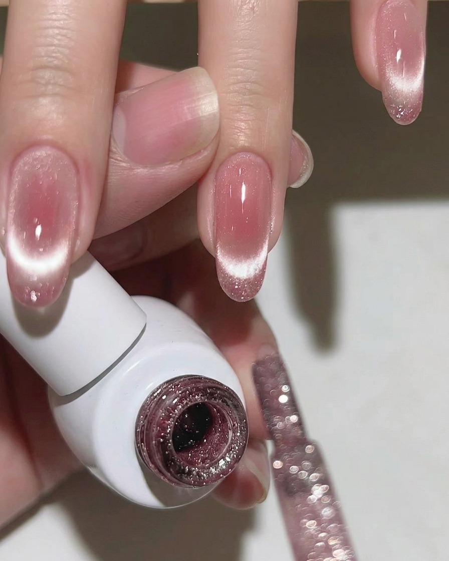 A close-up of a fingernail showing a vibrant, concentrated cat-eye shimmer line centered on the tip over a soft pink base.